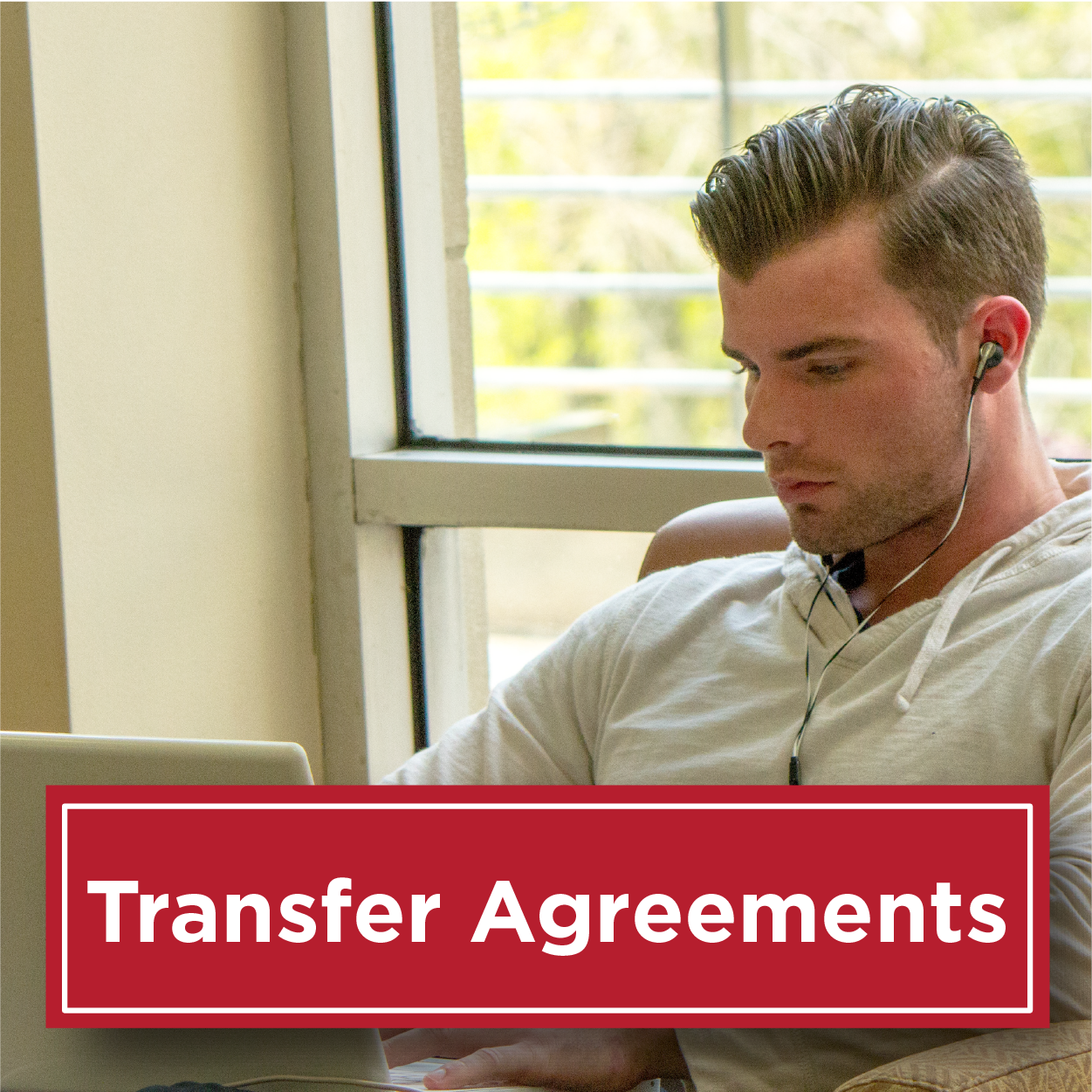 Photo of a male student sitting looking at his computer with headphones in his ears. Text reads transfer agreements