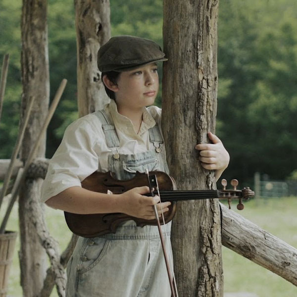 A boy standing on a wood pole holding an instrument in his hand.
