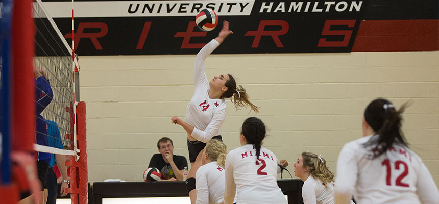  Women's Volleyball player jumping in the air to spike the ball over the net to her opponent.