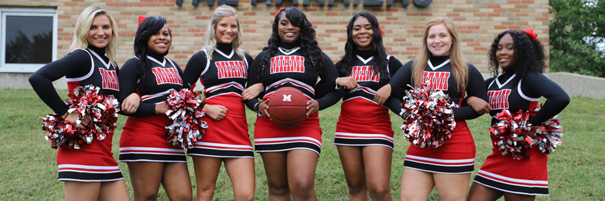  Hamilton cheerleaders standing in a line with the one in the middle holding a basketball. 