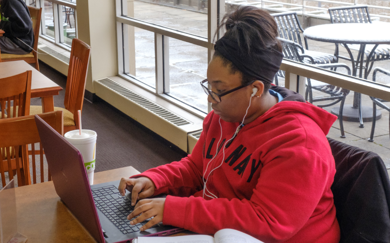 A student working on her laptop with headphones in. 