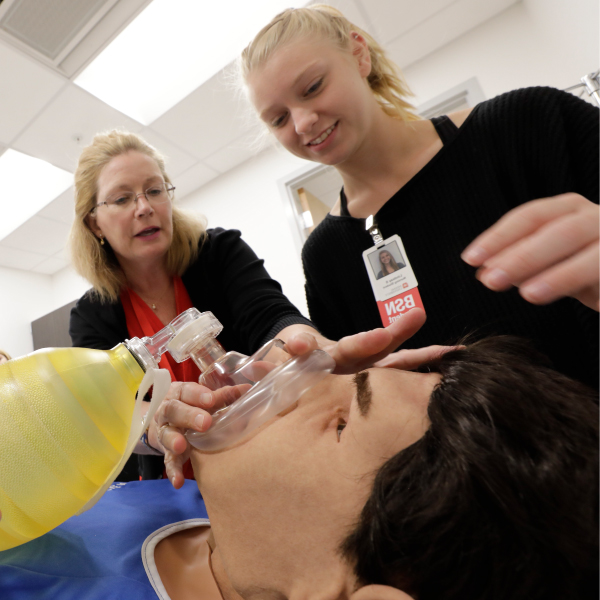 A nursing student working with a simulation mannequin while being instructed by a professor. 