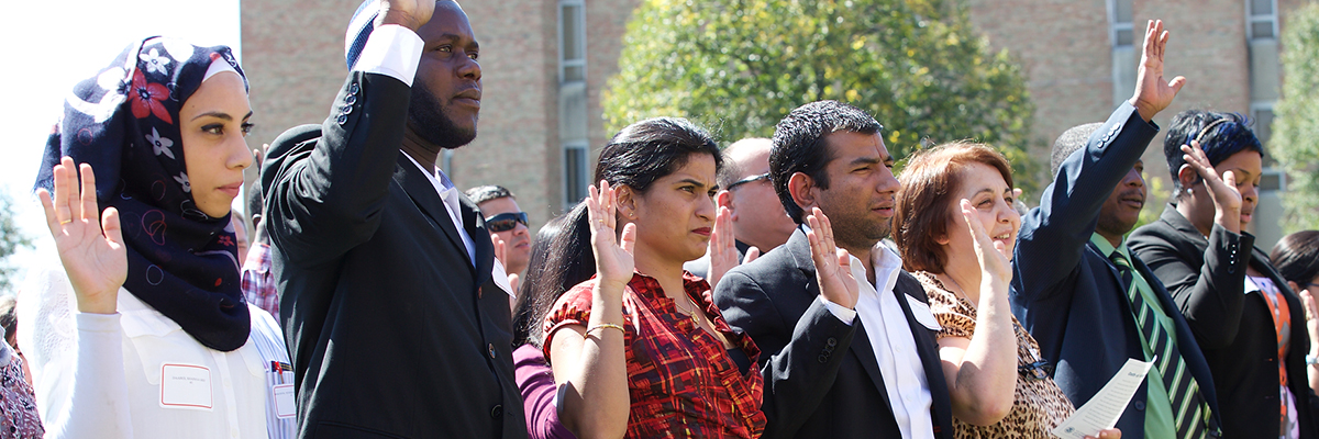Citizens at the Naturalization Ceremony on the Hamilton campus holding their right hands up. 