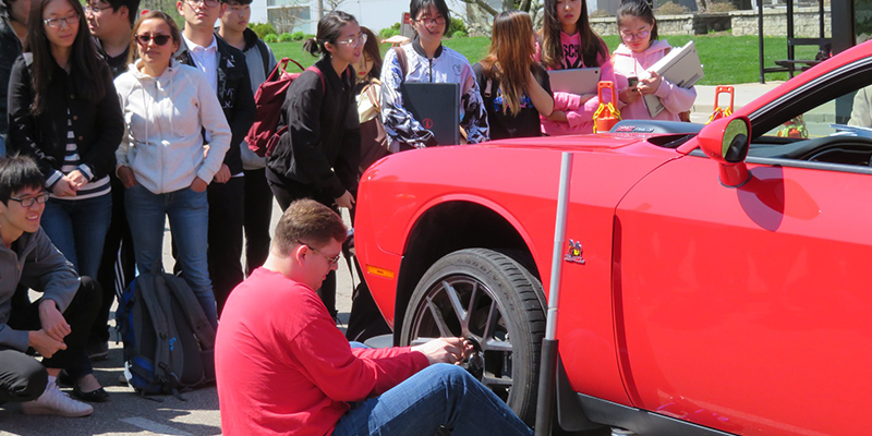 A instructor showing a group of students how to change a tire.  