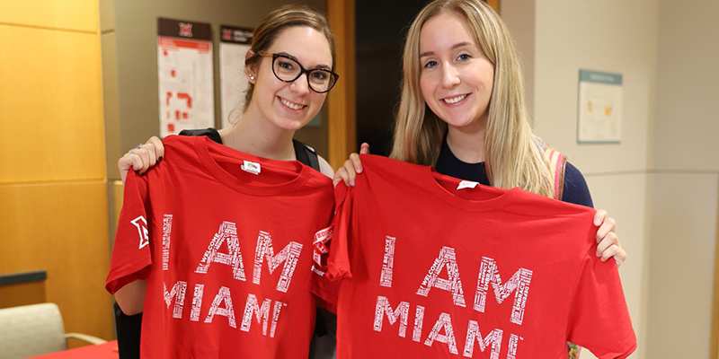  2 students standing with t-shirts in front of them with I am Miami.
