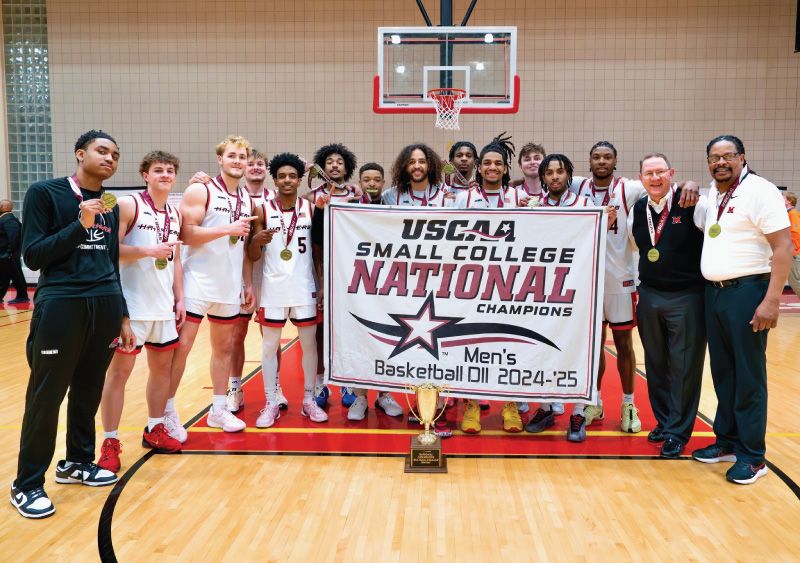 Miami Hamilton Harrier basketball team after winning the 2025 Men's Division II National Championship holding a banner.