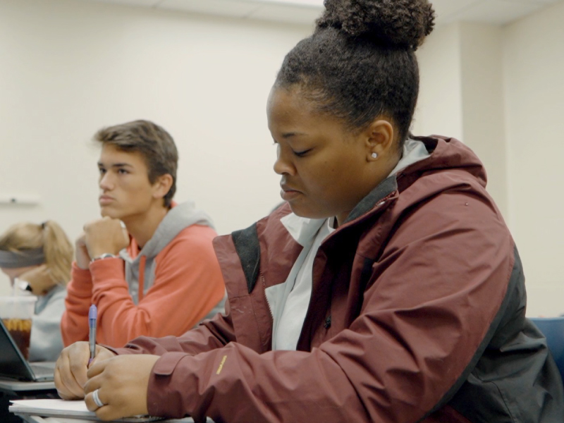 A student taking notes on a piece of paper during class.