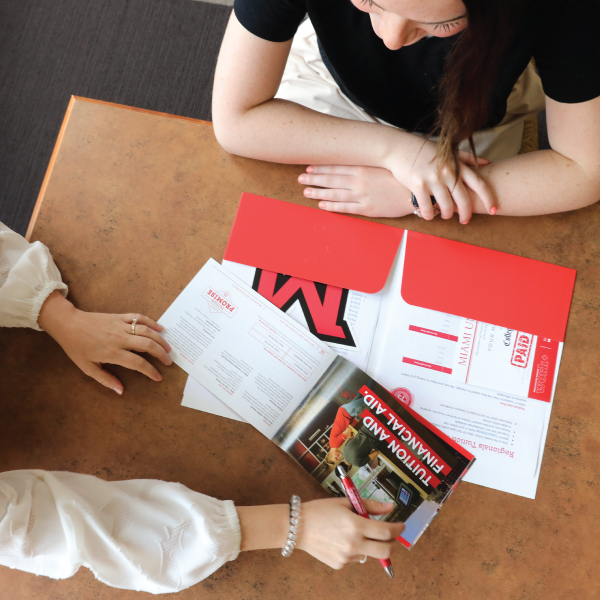 Miami Regionals admission material on a table with a counselor talking to a student.