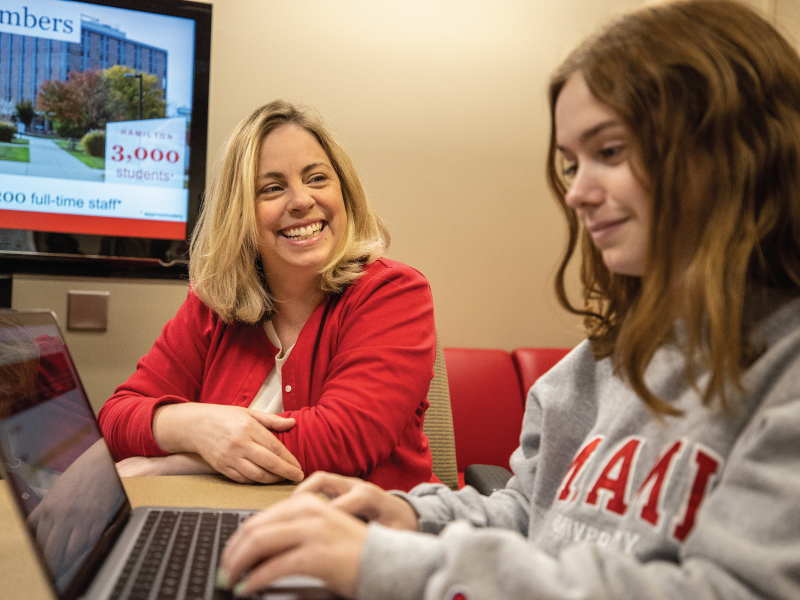 A admission counselor helping a prospective student fill out an application on their laptop.
