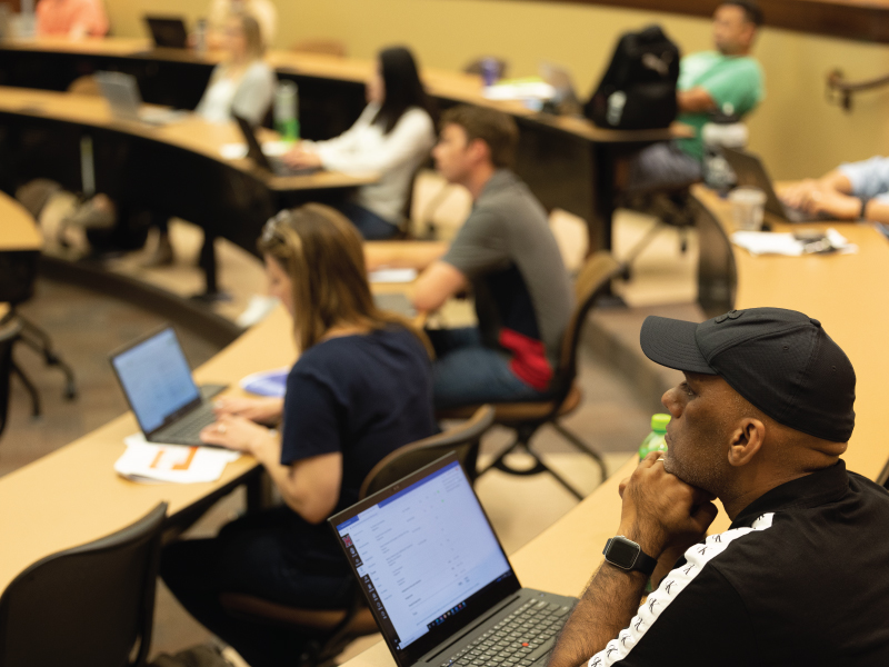 Students sitting in a classroom with their laptops in front of them.
