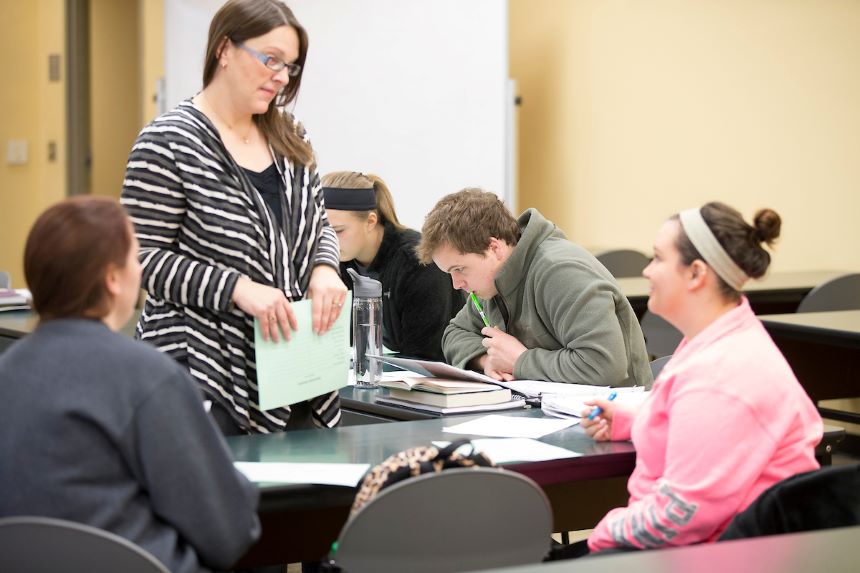 Professor stands next to a table of students.