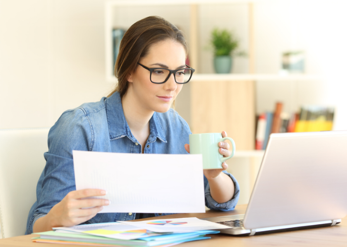 woman with a paper and coffee looking at her laptop