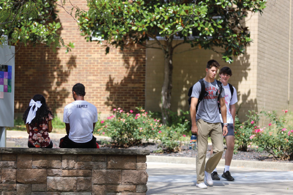 2 students walking out of Levey hall and 2 students sitting on a brick wall.