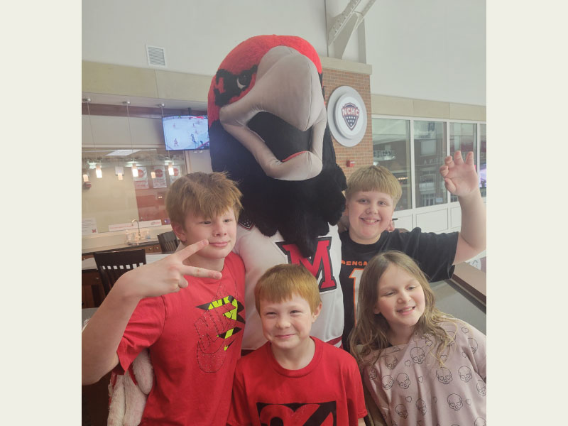 Littles of Big Brothers Big Sisters smile with Swoop during a Miami Redhawks hockey game.