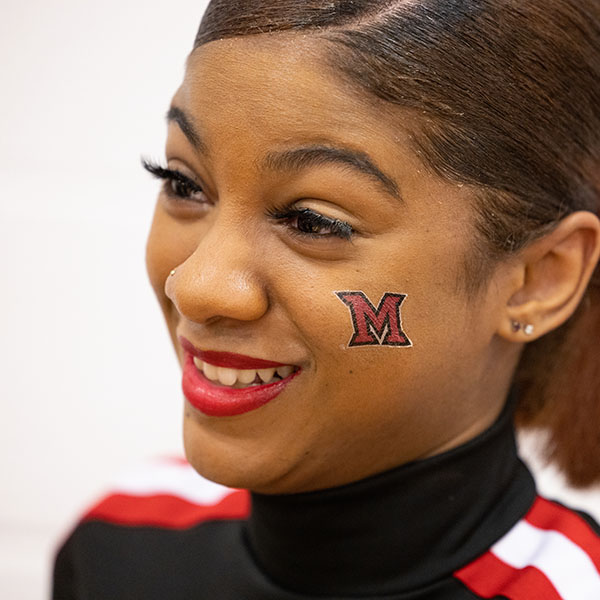 A cheerleader smiles with an M on her cheek