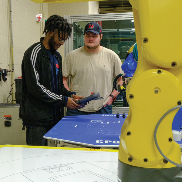 2 students using a remote to control a robot arm.