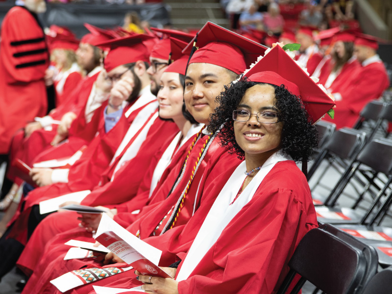 2 students sitting in their cap and gowns at graduation smiling