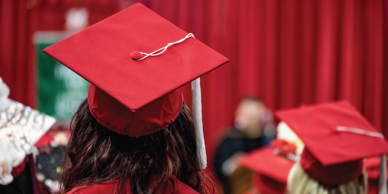 A student from behind in their graduation cap and gown sitting during the graduation recognition ceremony