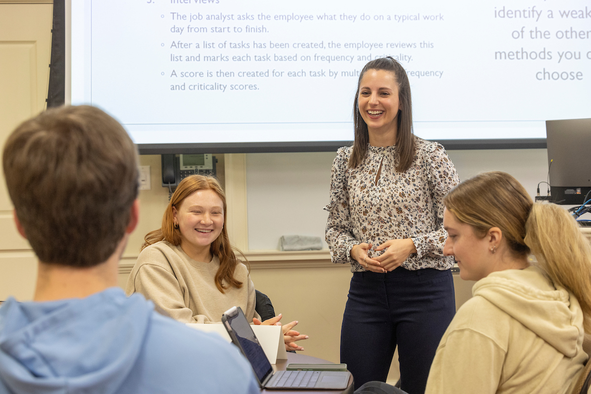 A professor smiles while speaking with four students.