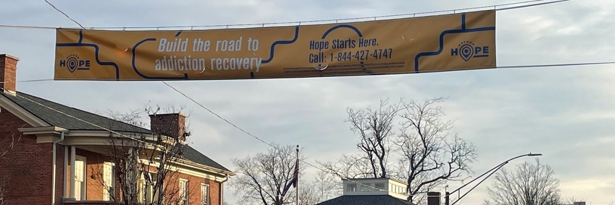 Large banner over high street that reads Build the road to addiction recovery. Hope Starts Here. Call 1-844-427-4747