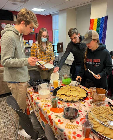Students in the Commuter Center gathering around a table of cookies and cookie decorating supplies