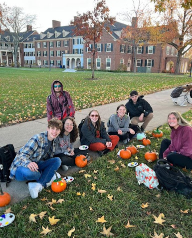 Commuter students sitting on central quad holding pumpkins and paint supplies