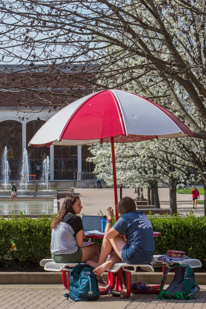 Spring day at Miami - two female students at an outdoor table with an umbrella over the table.