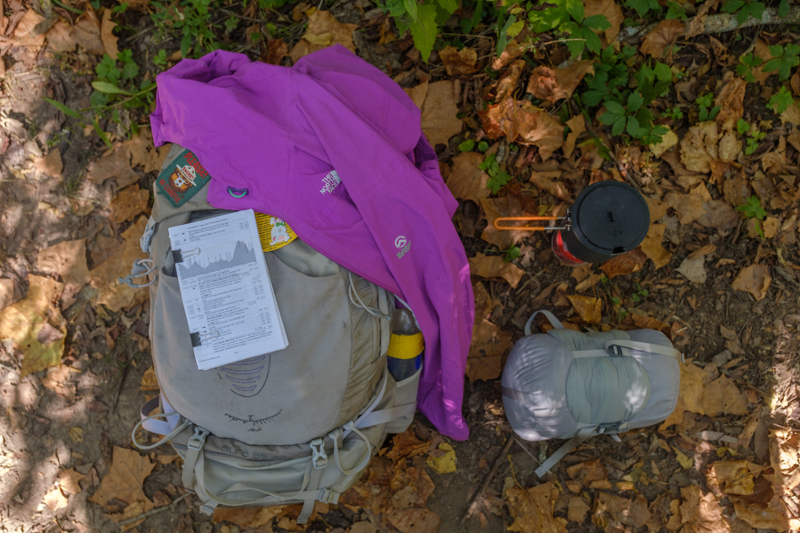 Backpack, jacket, waterbottle, and pack on a ground of fall leaves.