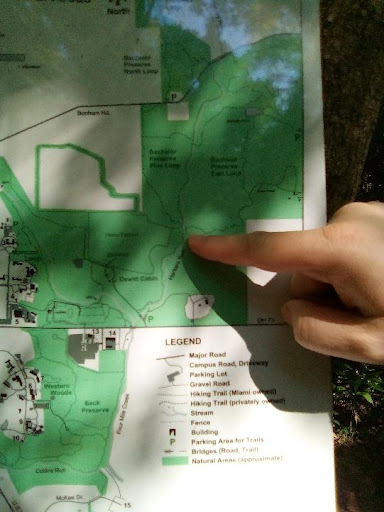 A hand pointing at a close-up sign with a map of the Miami University natural areas.