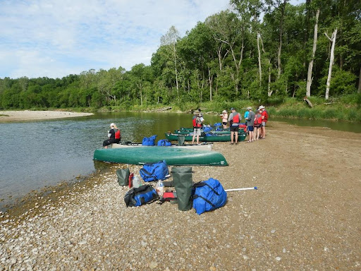 Group of students standing around 4 canoes on the shore of a river.