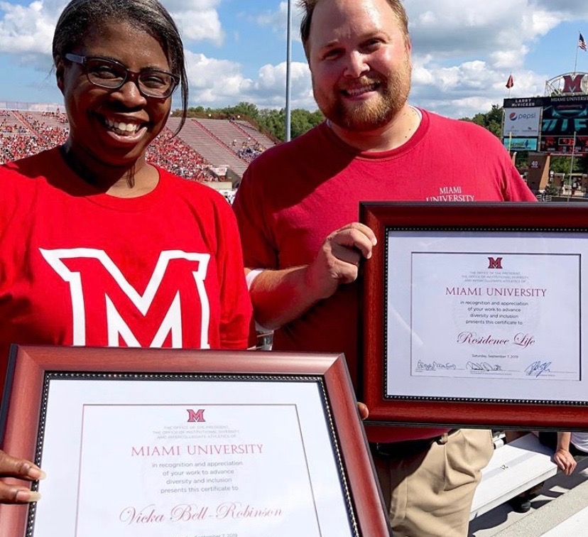 Vicka Bell Robinson and Jonathan James, of Residence Life, holding framed certificates at a football game