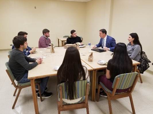 7 students, 1 faculty member seated and talking around a large square table