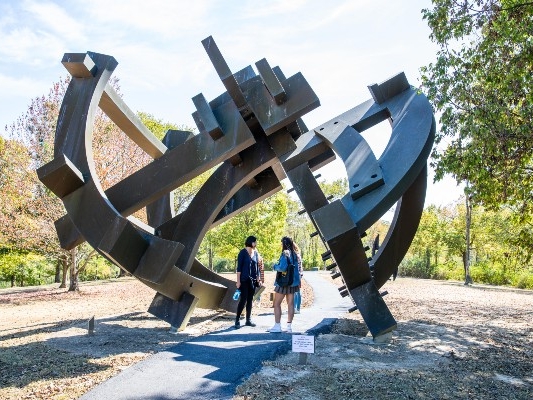  2 people standing under a large metal outdoor sculpture