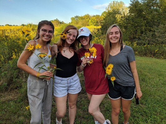  4 people outside posing for the camera, holding yellow flowers