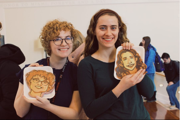 Two students holding up pancakes with their own faces at a Dancakes event. 