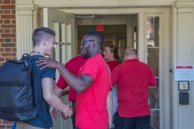  Miami person welcoming and shaking the hand of a new student walking into the residence hall on move-in day