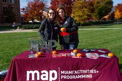 Two MAP students standing at a MAP table holding mini pumpkins at the 2017 Fallin' for Goggin