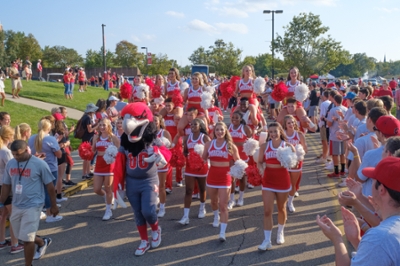Cheerleaders in uniform walking in Homecoming Hawkwalk with onlookers cheering on sidelines