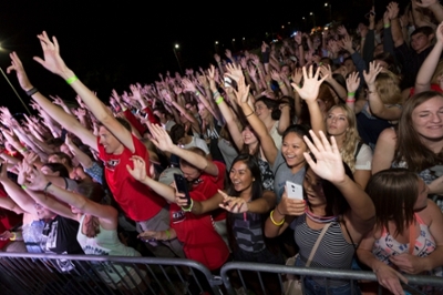 Large group of students with arms raised, dancing and singing at a concert