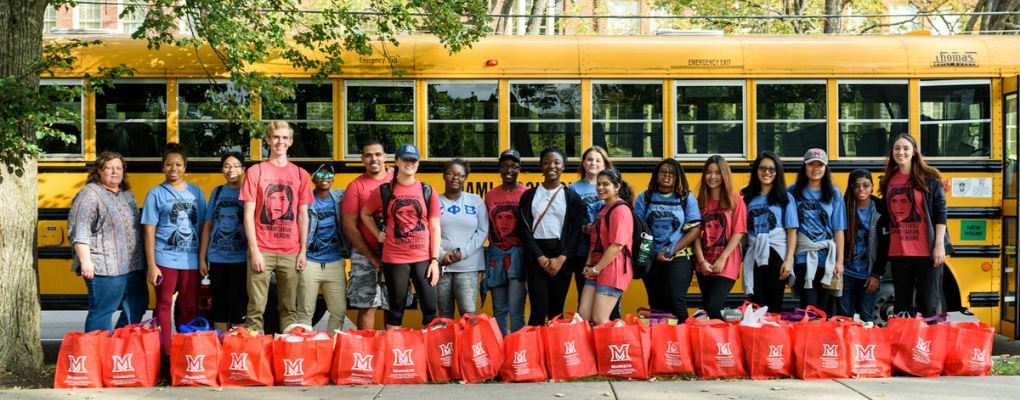 Group of students with hurricane relief supplies lined up in front of a yellow school bus