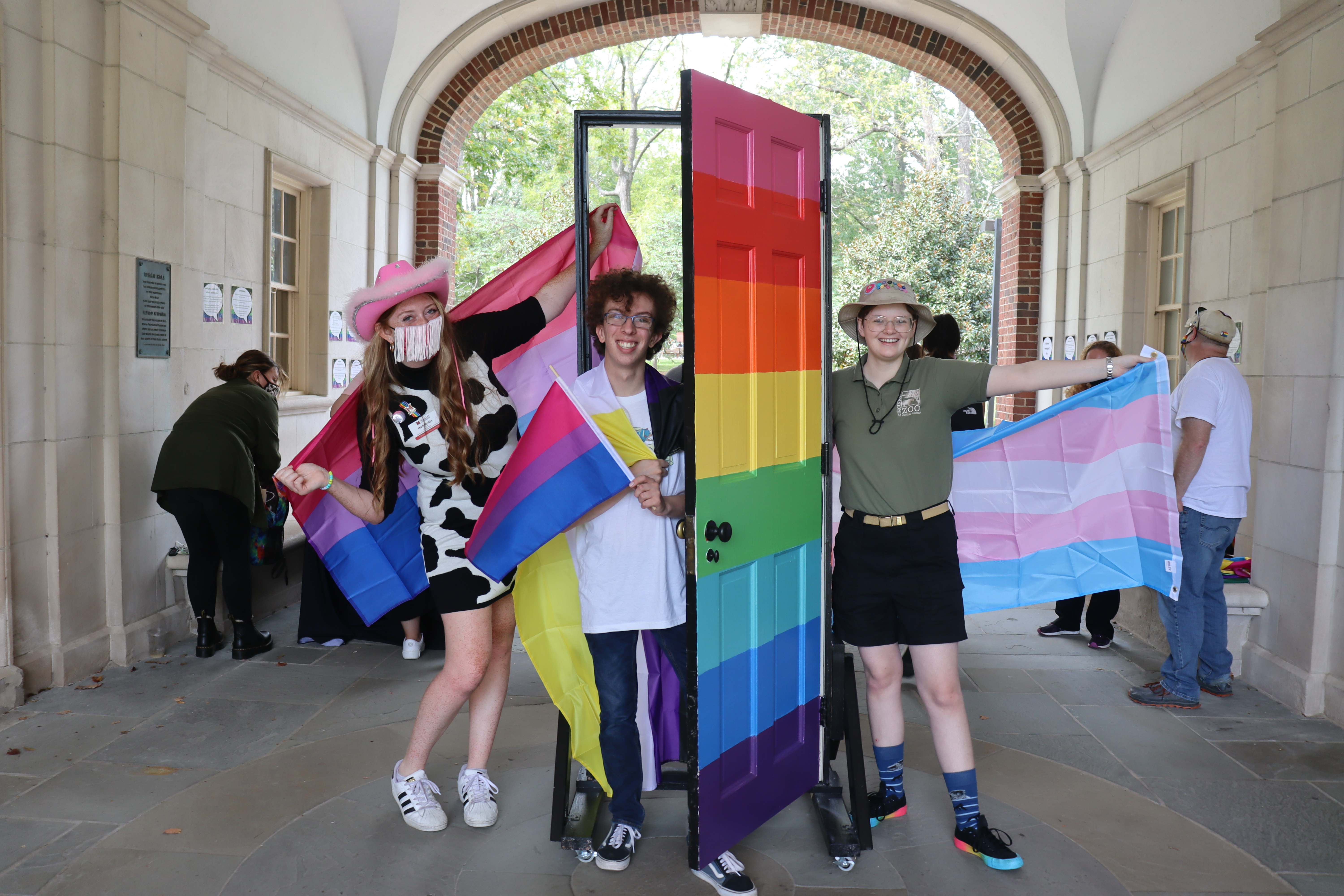 three students standing in front of a rainbow door