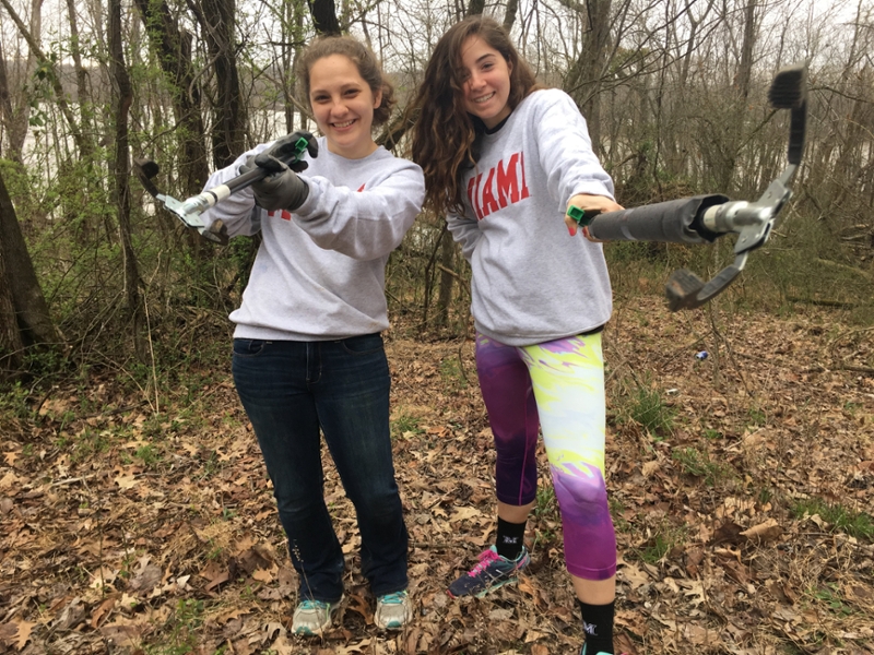 Two student participants in a RISE alt break, holding trash pickup tools.  