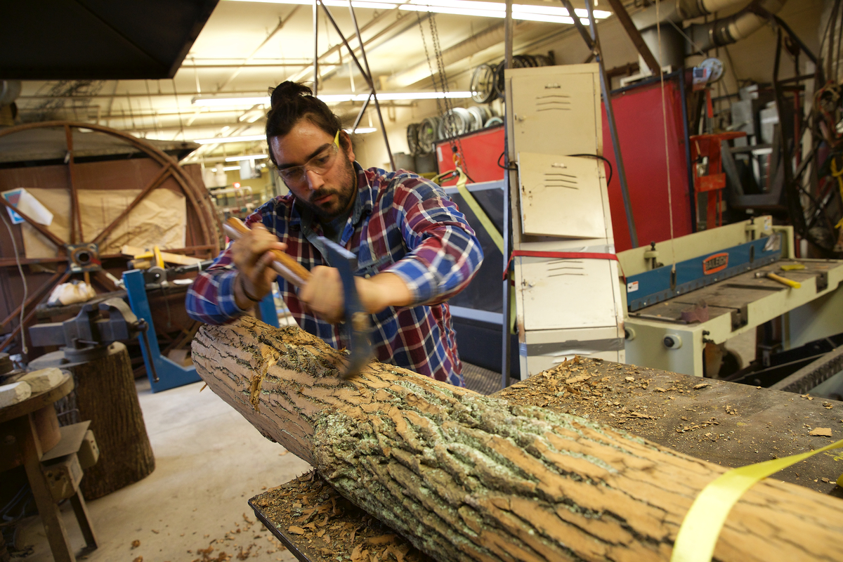 Student axing into a piece of wood as part of a sculpture class.