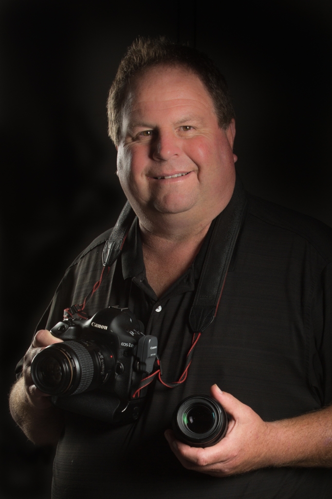 Portrait of Scott Kissell black background holding a camera and a lens