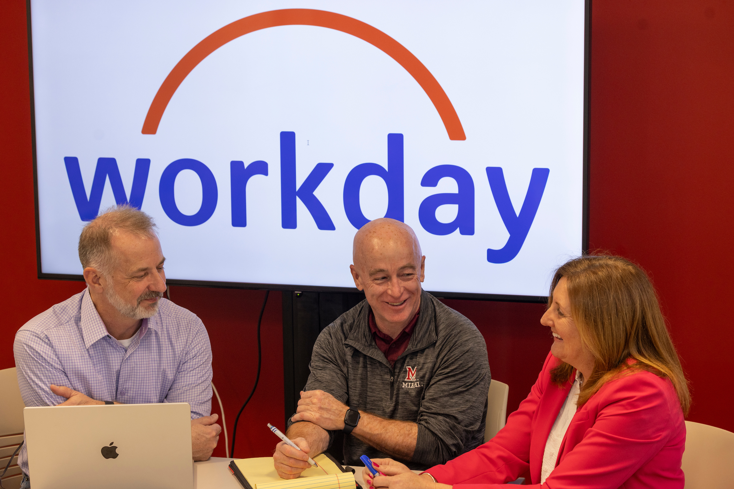 Three Miami staff members sit at a conference table with the Workday logo projected on a screen behind them.