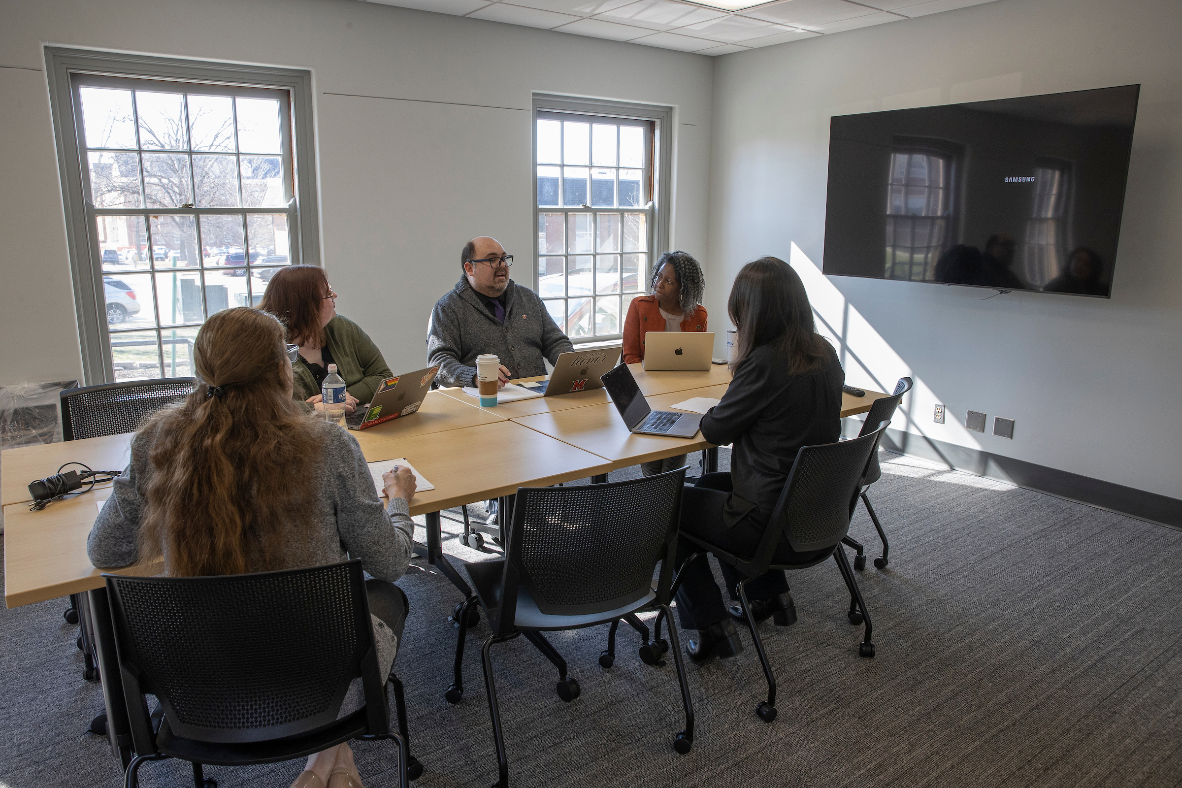 Miami staff members work together on a project, with two presenting to their seated colleagues.